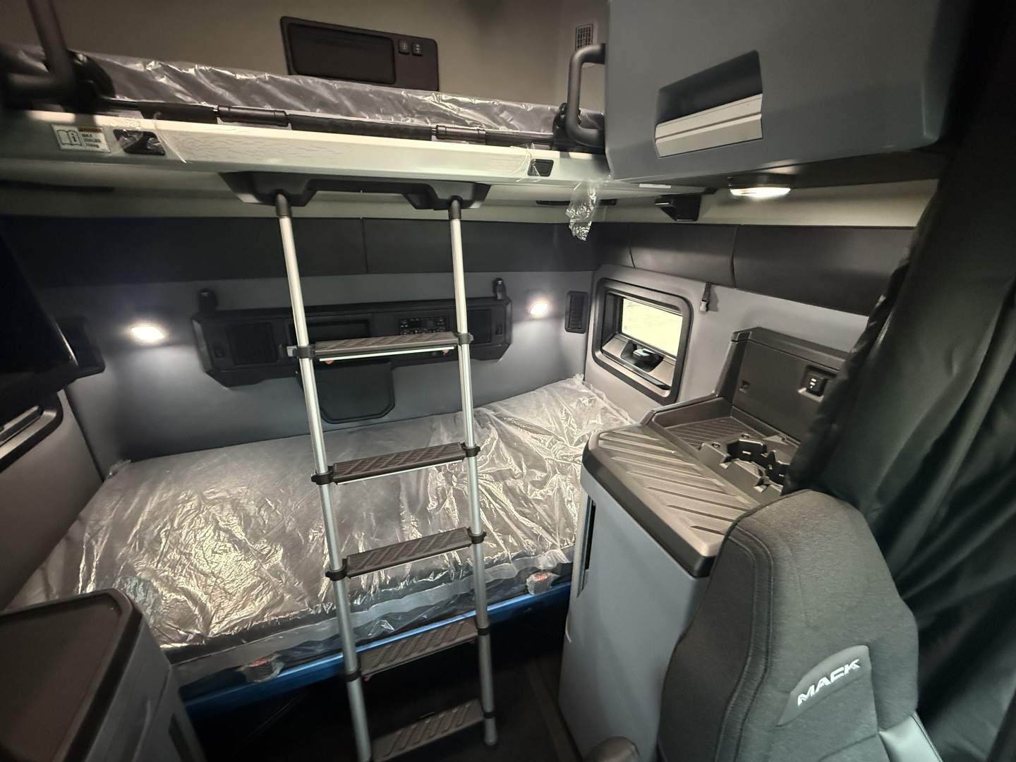 Mack PR64T76H sleeper cab interior showing bunk beds with ladder, overhead storage, window, and control console.