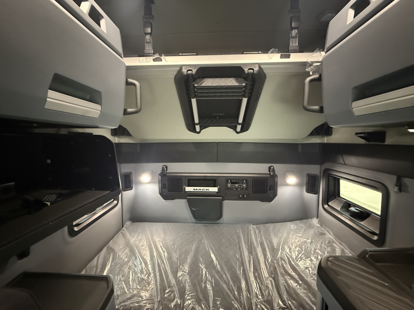 Mack PR64T76H sleeper cab interior showing overhead storage and control panel with vent and windows.