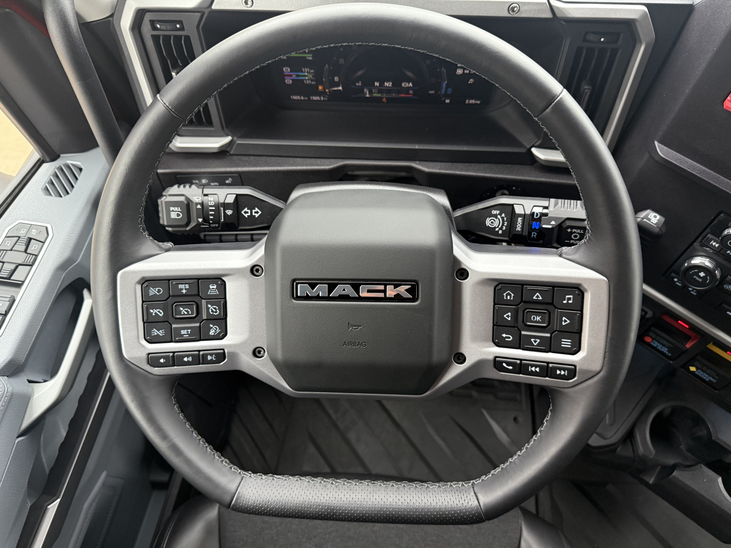 Steering wheel in a Mack truck cab showing integrated controls and dashboard display.