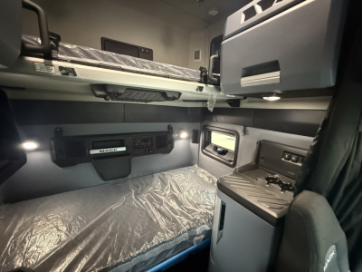 Truck cab interior of a new Mack PR64T76H sleeper showing bunk bed above storage and control panel with window and storage compartments.