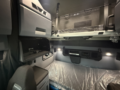 Interior cab of a Mack PR64T76H sleeper truck showing bunk area, overhead storage, dashboard with radio, and window shades.