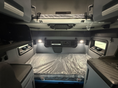Cab interior of a new Mack PR64T76H sleeper with bunk bed area and control panel.
