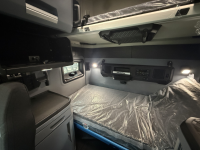 Mack PR64T76H truck interior bunk area with side cabinets and overhead storage, sleeper cab with plastic-covered bed and dim lighting.