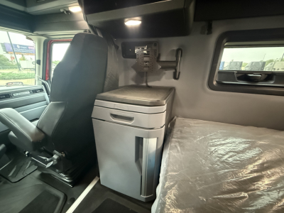 Mack PR64T76H sleeper cab interior showing driver's seat, console with storage, and bed area with plastic cover.