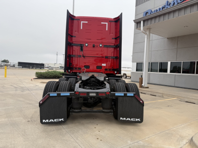  rear view of a red Mack PR64T76H truck cab with dual rear wheels, mudflaps labeled MACK, chassis and fifth wheel visible, in a dealership lot.