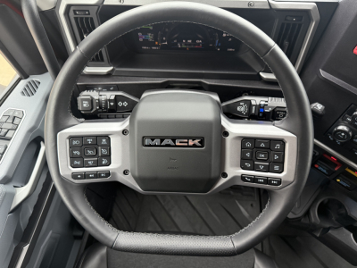 Steering wheel in a Mack truck cab showing integrated controls and dashboard display.