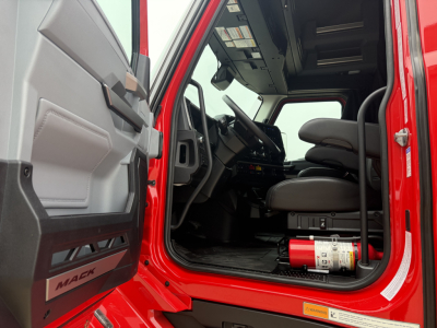 Mack PR64T76H truck cab interior showing driver seat and open door, with steering wheel and dashboard visible; red exterior and a fire extinguisher near the floor.