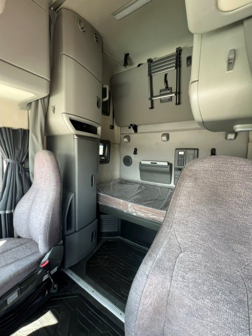 Volvo VNL64T760 sleeper cab interior showing bunk bed area and control panel. Includes passenger seat in foreground, overhead storage, and ladder/steps near window.