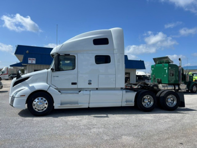 Volvo VNL64T760 sleeper cab truck side view showing white tractor with aerodynamic roof fairing and chrome wheels.