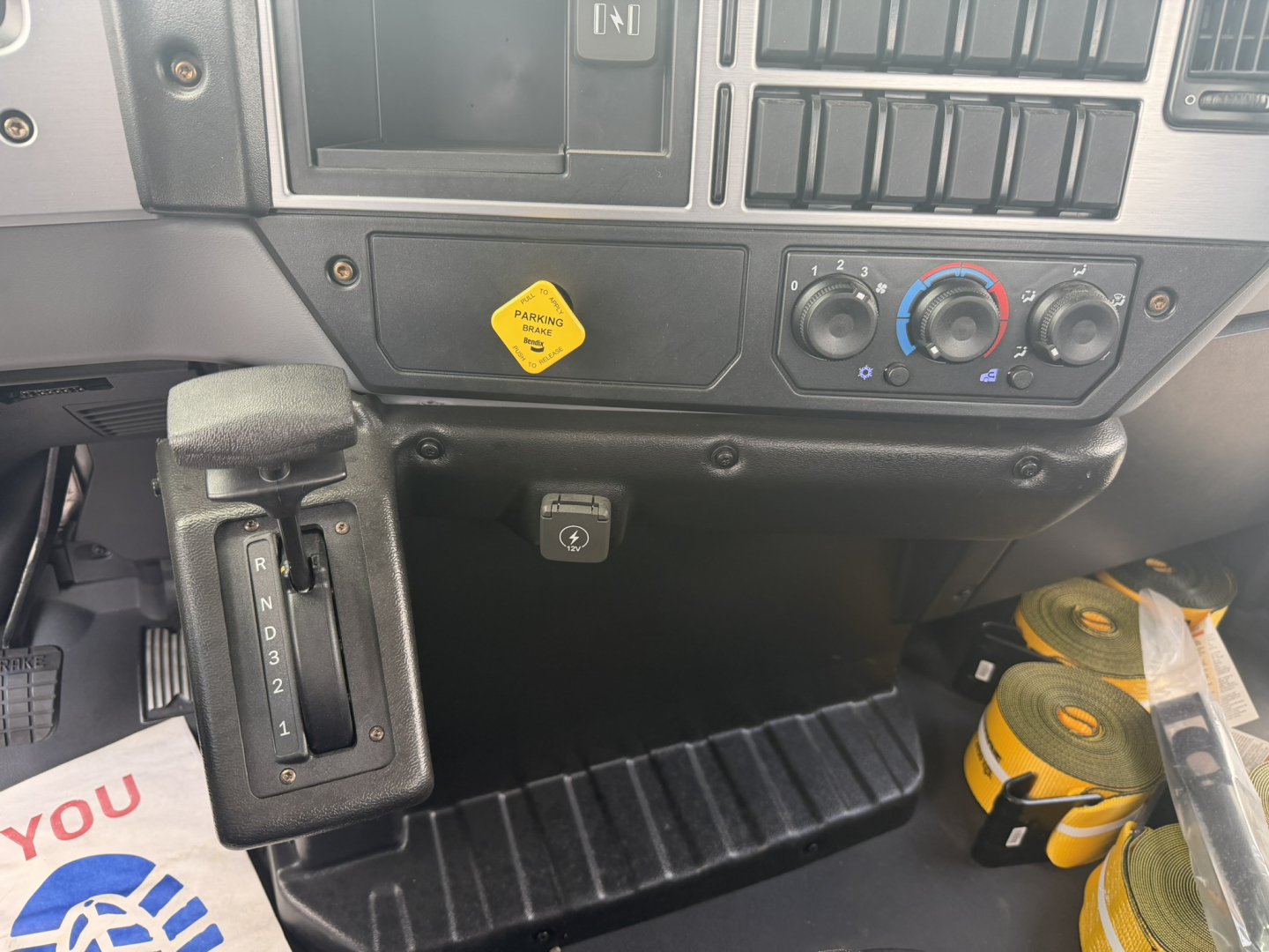 Dashboard of 2026 Mack MD6 with gear selector on left, climate controls, and yellow warning sticker.