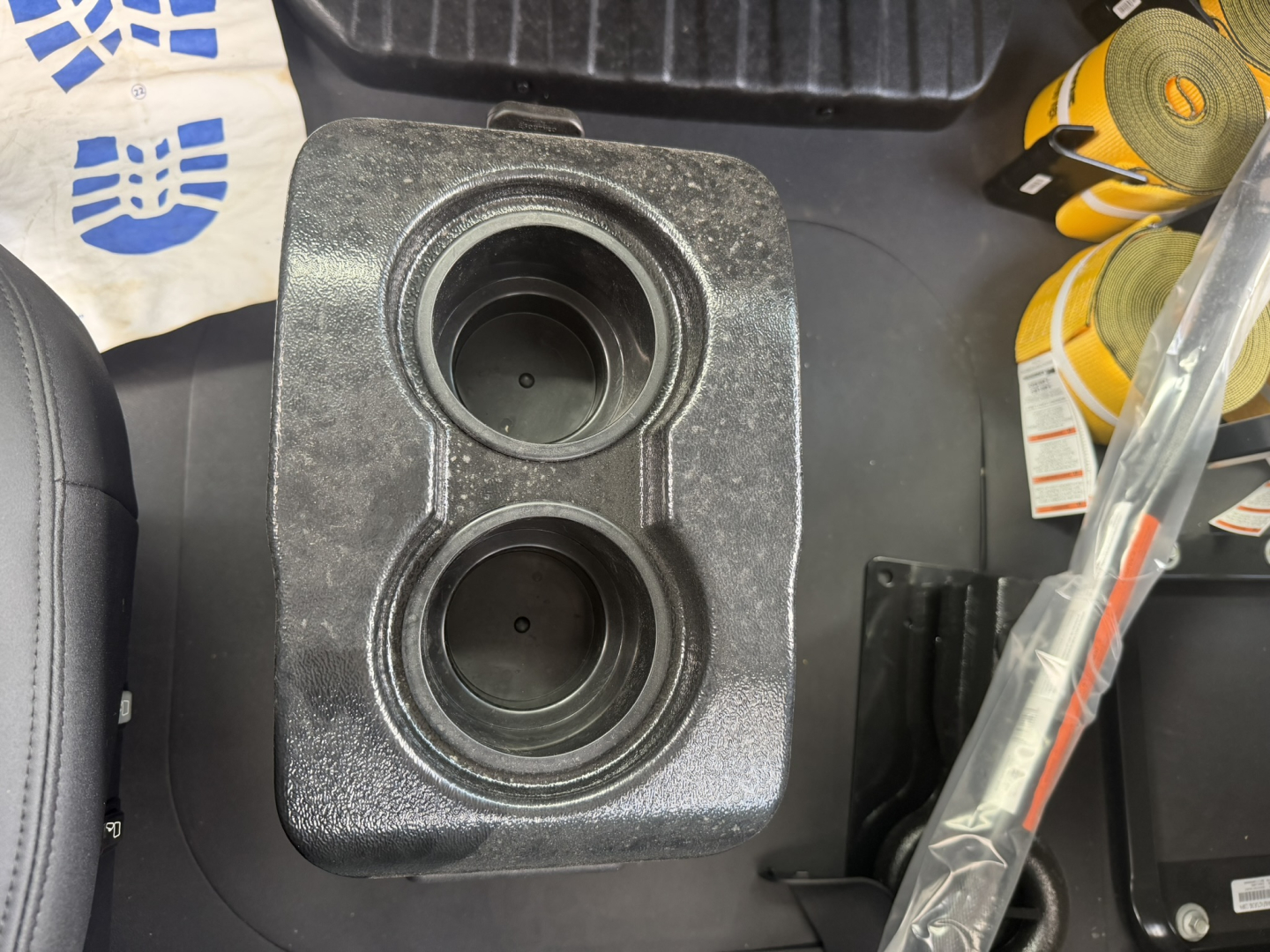 Twin cupholders in a metallic console/console insert with circular openings; part of a truck interior accessory, with a strip of masking tape and tools nearby.