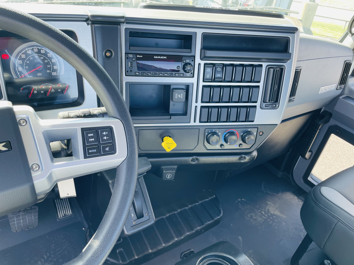 Mack MD6 dash and center console showing digital radio, climate controls, and dashboard switches; steering wheel left; instrument cluster visible.