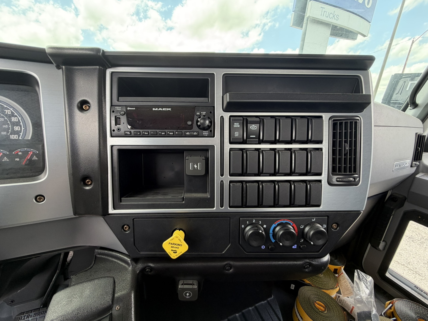 Dashboard of a 2026 Mack MD6 flatbed truck showing radio, climate controls, multiple switches, and yellow hood release handle.