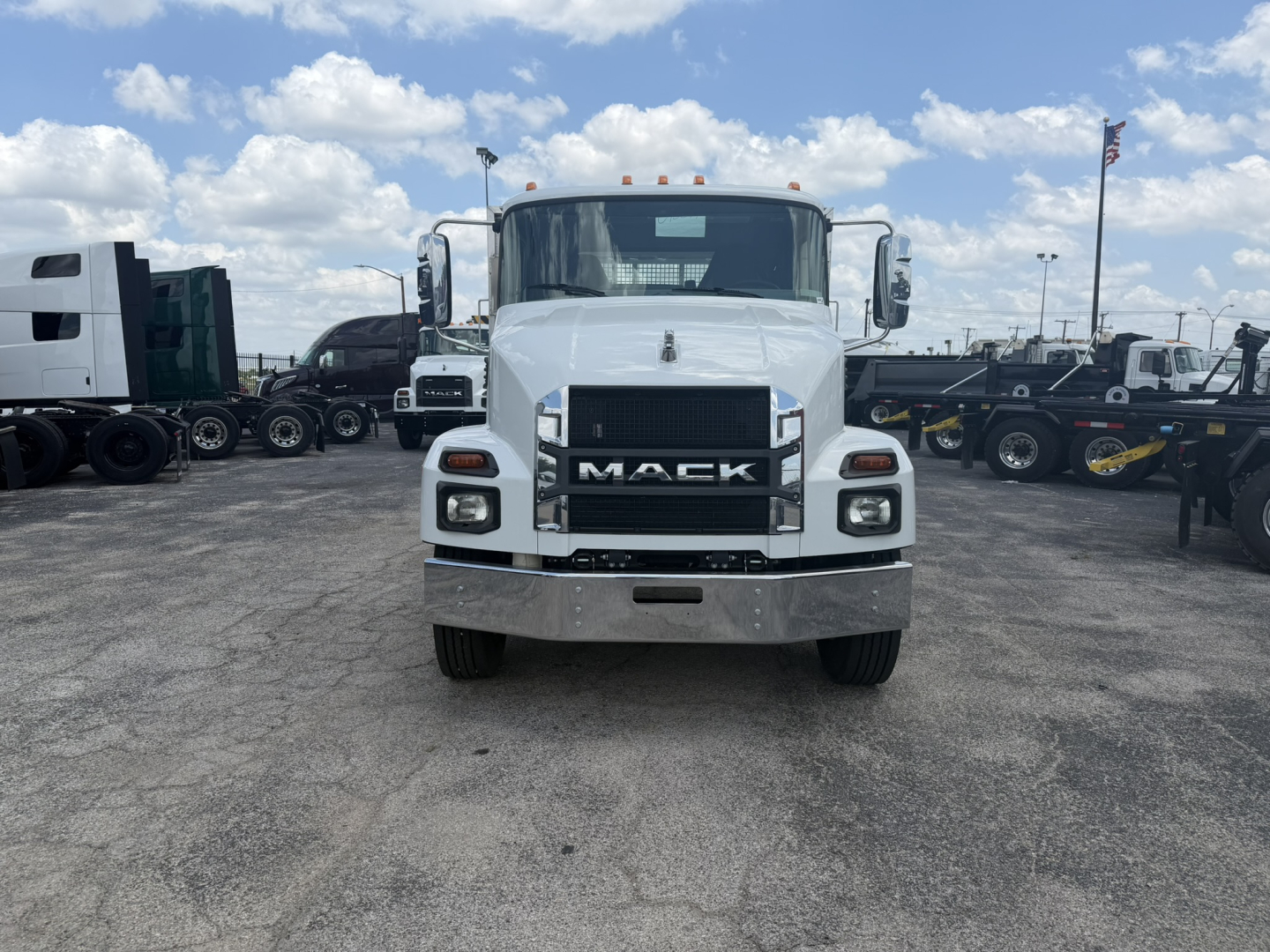 Front view of a white 2026 Mack MD6 flatbed truck showing grille, bumper, headlights, and Mack emblem.