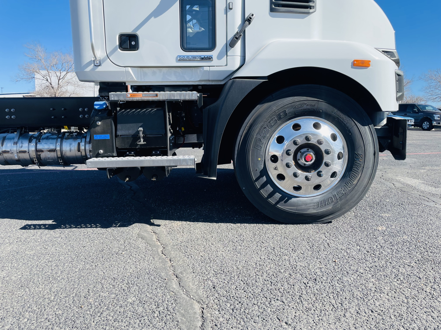 Mack MD6 cab and front wheel area showing wheel, tire, steps, and fuel/air lines; side view of truck with chassis components visible.
