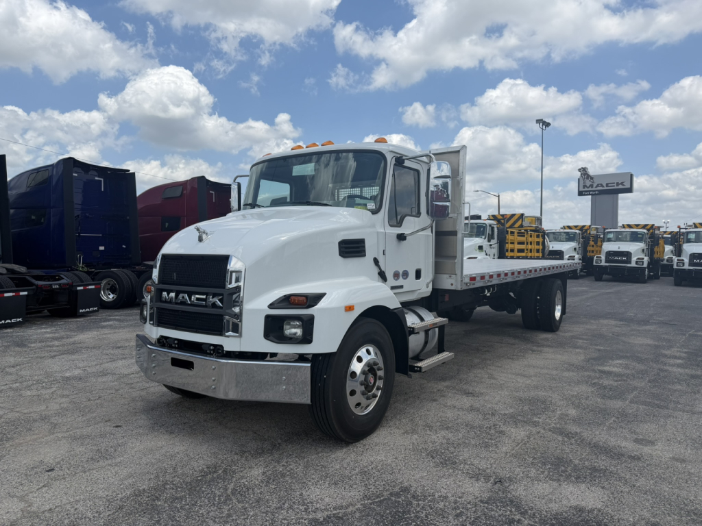 Mack MD6 flatbed truck in a dealership lot, white cab, chrome front bumper, with flatbed and yellow safety beacon lights on cab roof.