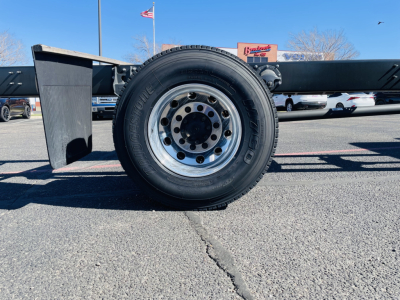 Flatbed truck wheel and undercarriage showing large steel wheel with radial tire, hub, and chassis frame stub, 2026 Mack MD6 listing in background.
