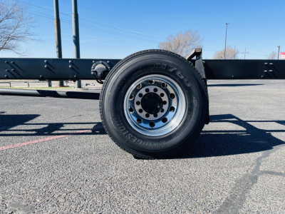 Front tire and frame of a Mack MD6 flatbed truck showing tire with M+S wheel and suspension components.