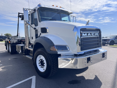 Mack GR64B heavy duty truck front-left view with large chrome bumper and grille showing 'MACK' on the grille, white cab, black front wheel well, and side exhaust stack visible.