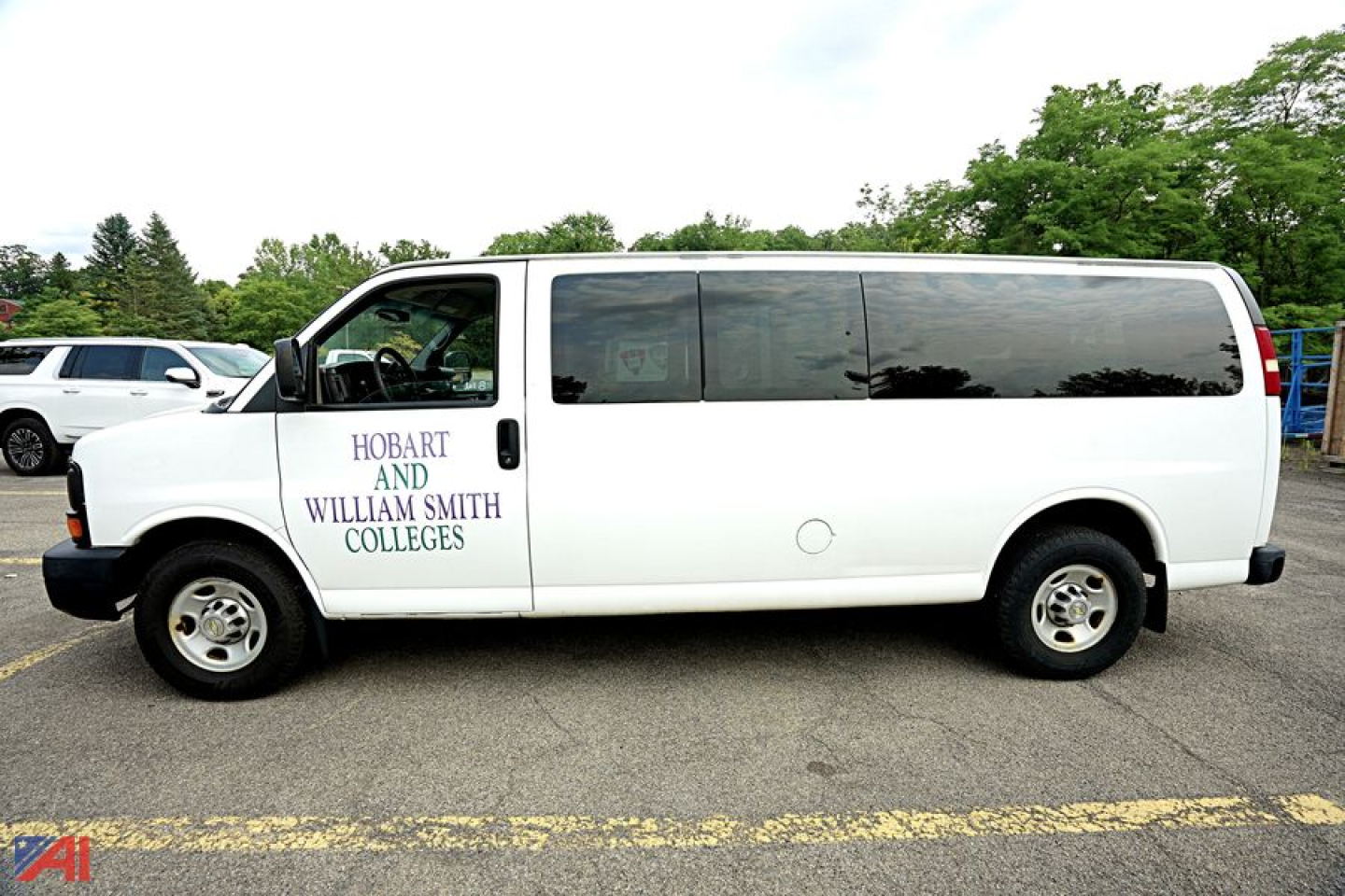 Van side view: white 2014 Chevrolet Express 3500 passenger van with dark tinted windows and logos on front door reading HO BART AND WILLIAM SMITH COLLEGES.