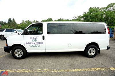 Van side view: white 2014 Chevrolet Express 3500 passenger van with dark tinted windows and logos on front door reading HO BART AND WILLIAM SMITH COLLEGES.