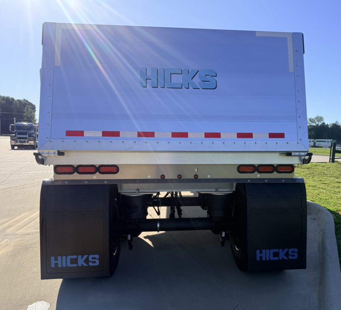 Hicks dump trailer rear view showing large metal tailgate with Hicks logo, dual rear axles, black mud flaps labeled HICKS, and red/white reflective tape.