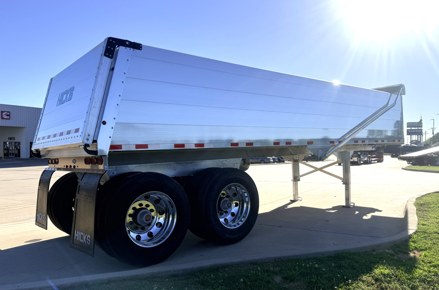 Hicks FL2827 dump trailer on roadside, dual rear axles, aluminum cargo bed, reflective tape, and landing legs visible.