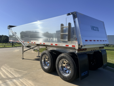 Hicks dump trailer with polished aluminum side, dual rear wheels, and ladder on front panel showing HICKS logo.