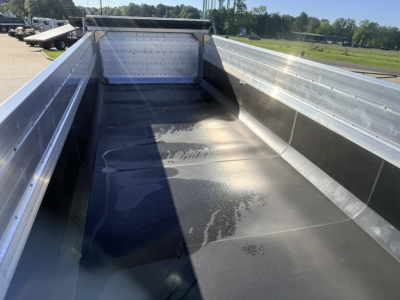 Dump trailer bed with aluminum side rails and smooth black-coated floor, inside view showing open-top cargo area and front bulkhead.