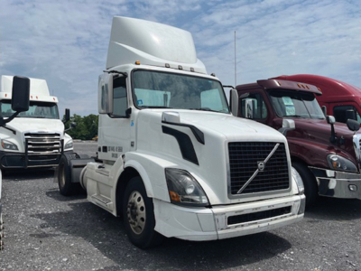 Volvo VNL 300 daycab tractor front view showing large grille, headlights, white paint, and other trucks in background.
