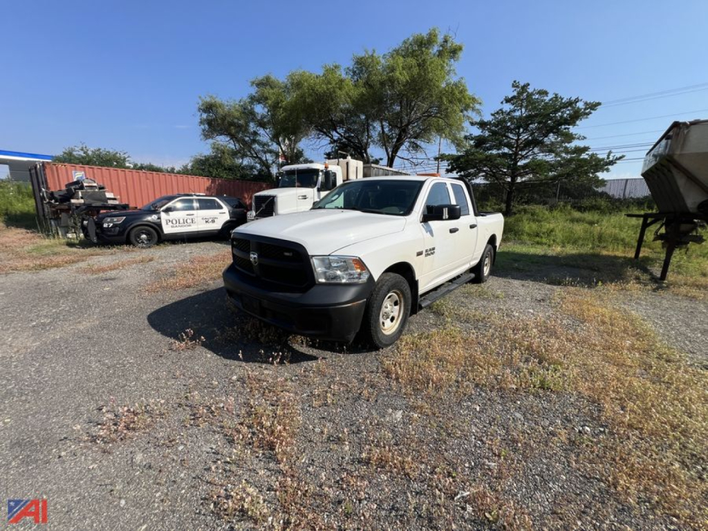 Ram 1500 Tradesman crew cab pickup truck in white, front view in a gravel lot with other vehicles and equipment in background.