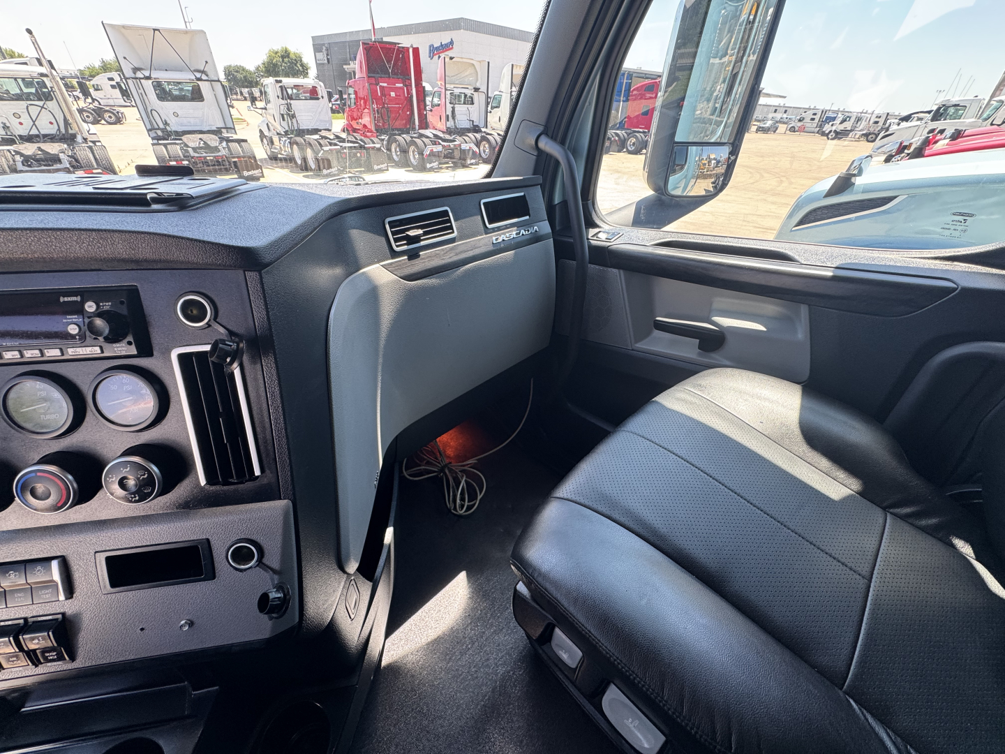 Freightliner Cascadia 126 cab interior view showing dashboard gauges, steering wheel, passenger seat, and side window.