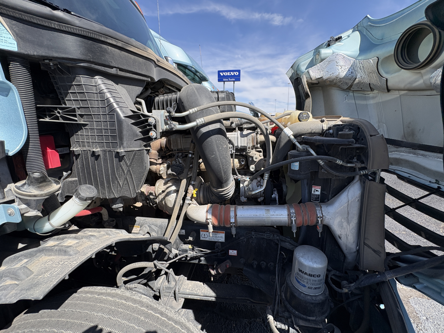 Truck engine bay of a 2023 Freightliner Cascadia 126 showing radiator, hoses, air filter housing, and assorted engine components from a front-right perspective.