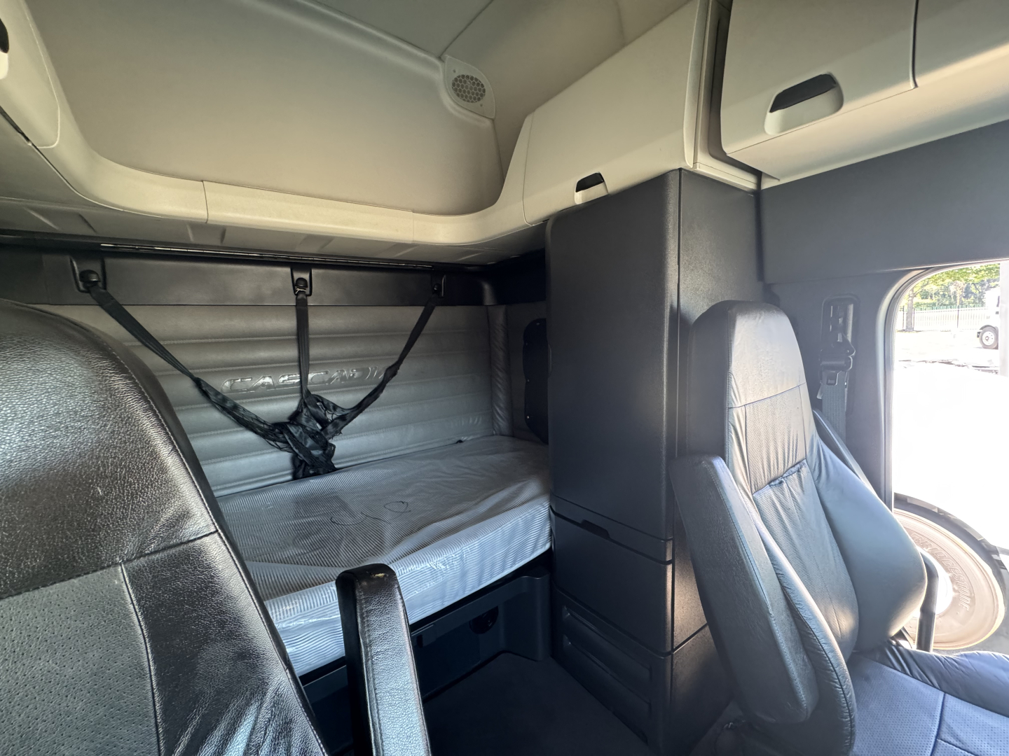 Cab interior of a Freightliner Cascadia 126 sleeper showing bunk bed with storage, upper and lower berths, and driver seat.