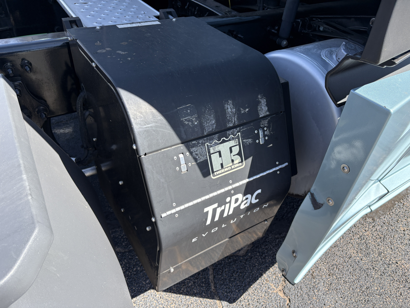 Trapped air intake or battery box labeled Tripac Evolution under the cab of a Freightliner Cascadia 126; black metal housing with Tripac Evolution logo.