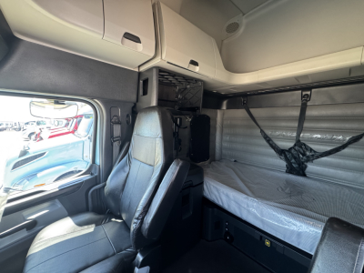 Cab interior of a 2023 Freightliner Cascadia 126 sleeper showing upper bunk storage cabinets, side wall, and driver seat.