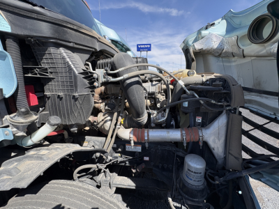 Truck engine bay of a 2023 Freightliner Cascadia 126 showing radiator, hoses, air filter housing, and assorted engine components from a front-right perspective.