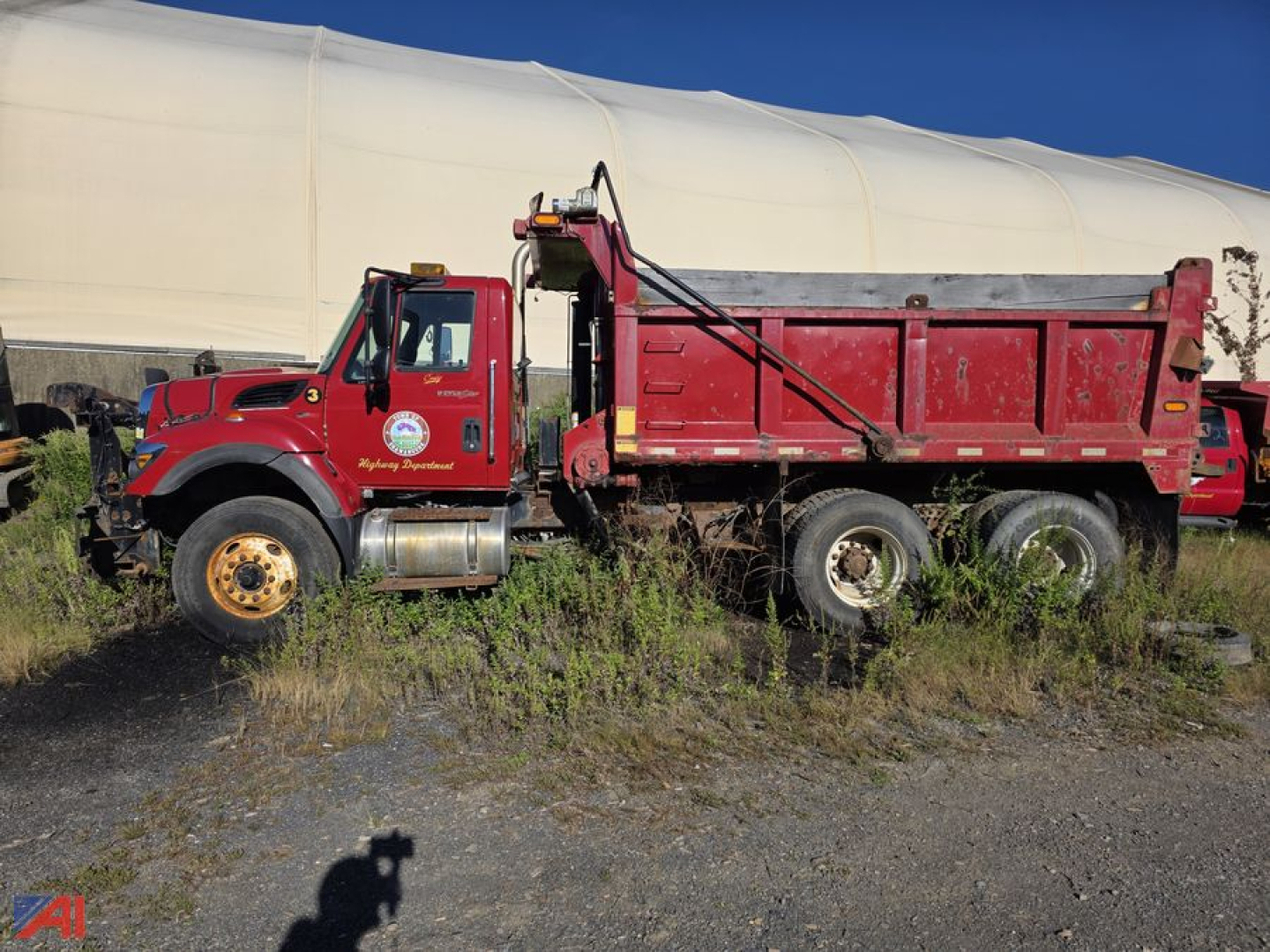 Truck: 2009 International WorkStar 7500 dump body with sander. Red cab and dump bed, logo on door, dual rear axles, large tires, side rails, in-field view.