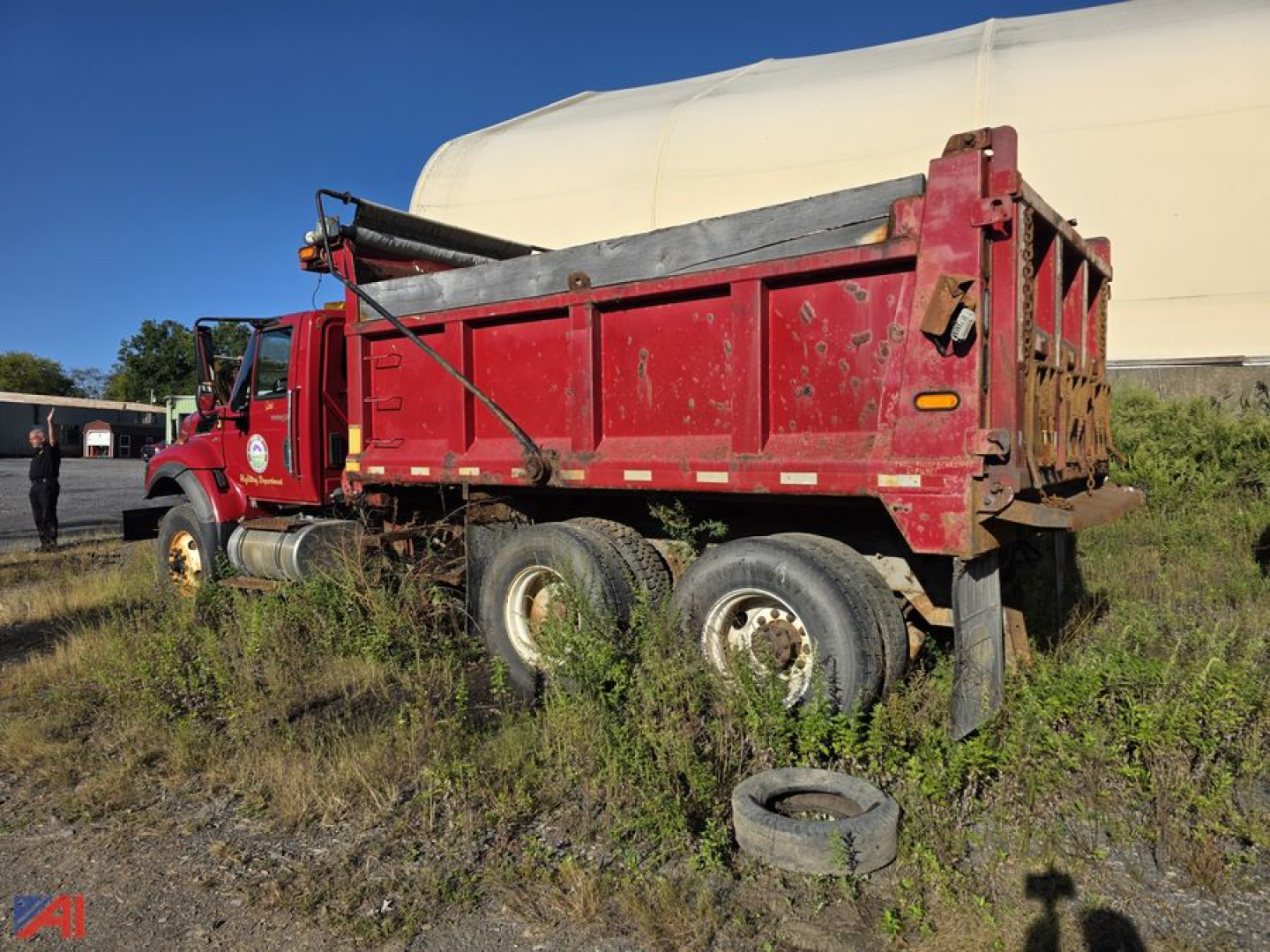 Dump truck showing red International WorkStar 7500 with sander body, side view, tires and overgrowth around the chassis.