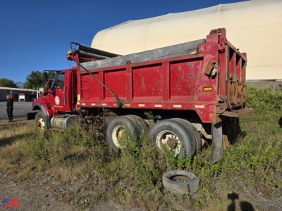 Dump truck showing red International WorkStar 7500 with sander body, side view, tires and overgrowth around the chassis.