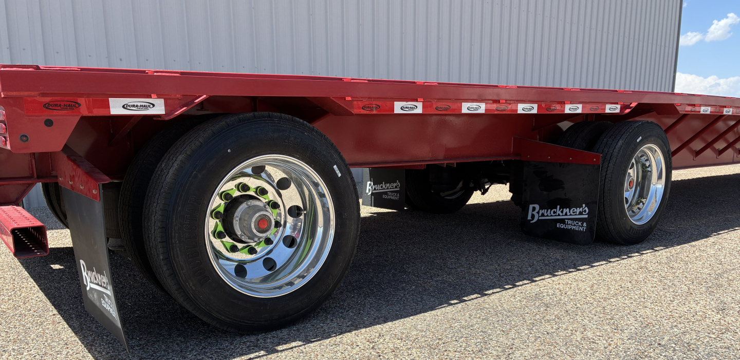 Trailer wheel trio: red drop deck trailer with dual rear axles, polished chrome rims, black mud flaps, and white reflective branding along the edge.