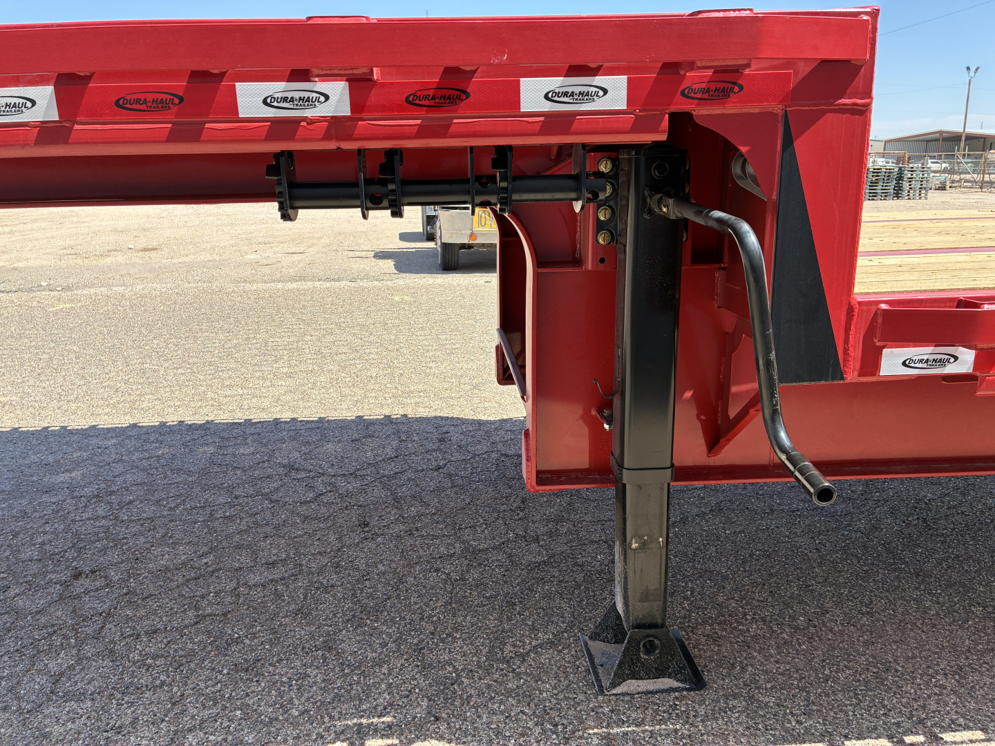 Red Dura Haul drop deck trailer fender area showing adjustable landing gear and hydraulic/hose components.
