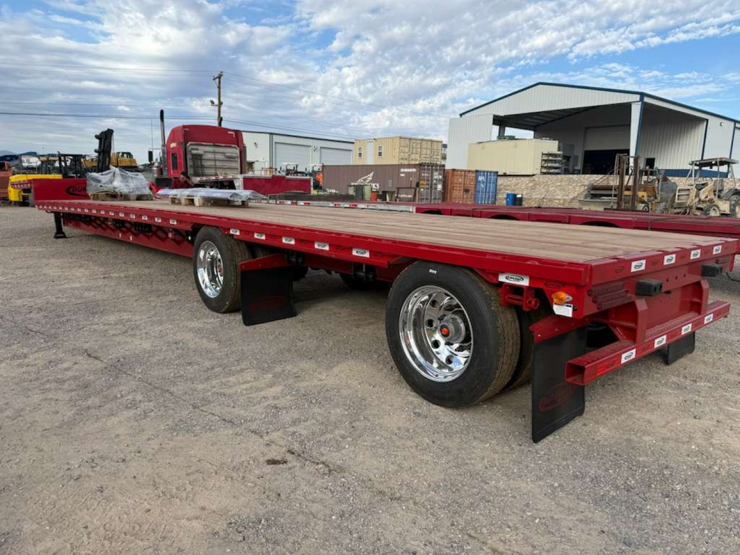 Trailer: red 53' drop deck spread trailer with dual rear axles and chrome wheels, flatbed with side rails, in a yard.