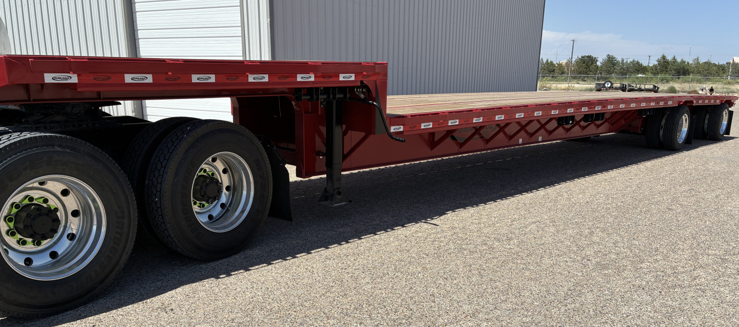 Trailer side view showing a red 53' drop deck spread trailer with dual rear axles and flatbed deck.