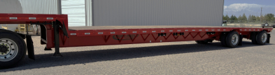 Trailer side view showing red 53' drop deck trailer with triple-axle rear, low ground clearance, and gooseneck hitch in front.