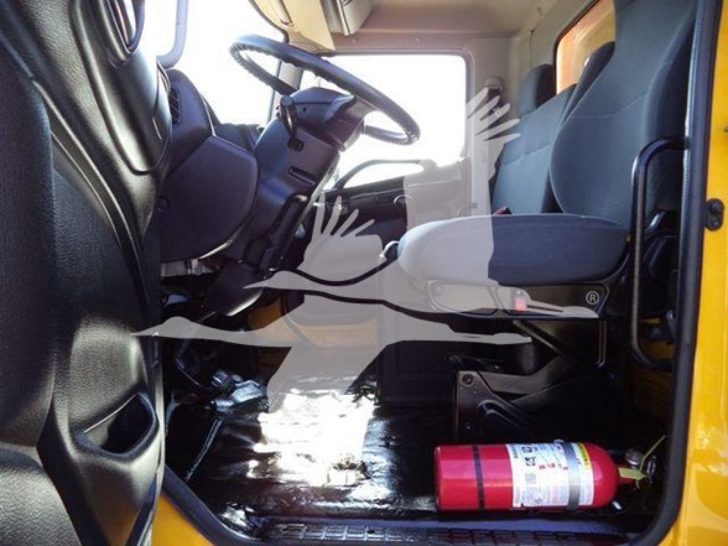 Interior cab of a 2019 Hino 268A with steering wheel, driver seat, and emergency fire extinguisher mounted near the door, showing the dash and pedals.