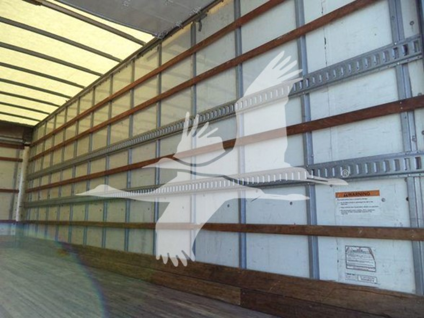 Truck trailer interior with side wall text and warning labels visible; no detailed model text legible.