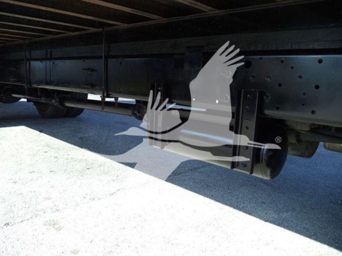 Underbody view of a box truck chassis showing a reinforced frame rail and leaf spring suspensions with a visible axle area.