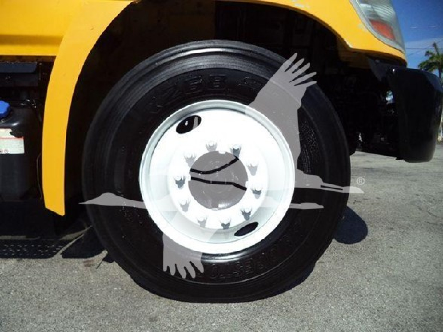 Wheel close-up showing black tire with white rim on yellow truck, hub-center with bolts visible.