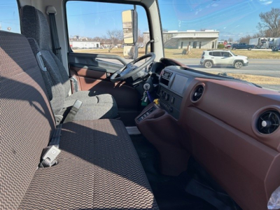 Interior cab view of a new 2025 Hino L6 cab and chassis showing brown dashboard, steering wheel, and bench seat; seating and instrument panel visible.